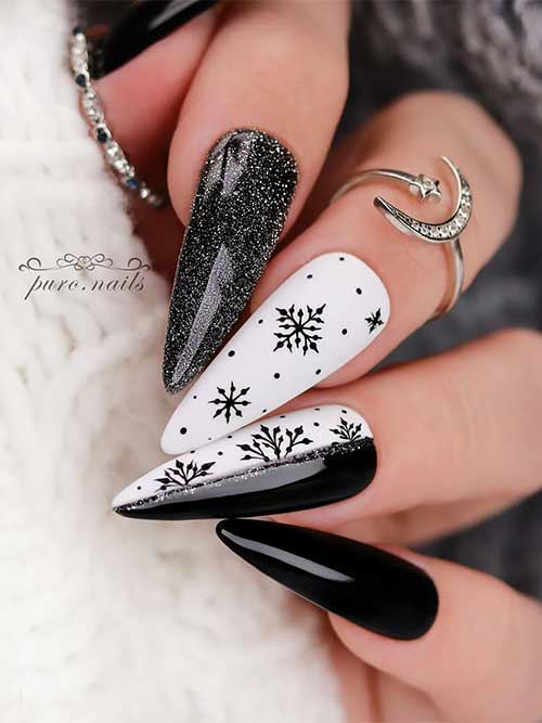 Uñas largas en blanco y negro con brillo plateado, copos de nieve negros en dos uñas blancas decorativas, una de ellas mitad blanca y mitad negra.