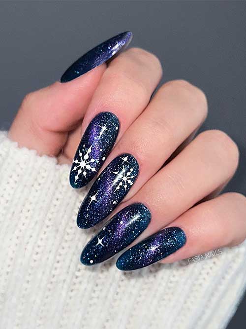 Uñas largas y negras con brillo que recuerdan a una galaxia. Además, un toque de estrellas moradas y blancas, y grandes copos de nieve.