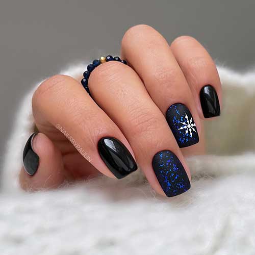 Uñas cortas de invierno negras con dos uñas negras decorativas con copos azules y un gran copo de nieve blanco en la uña anular.