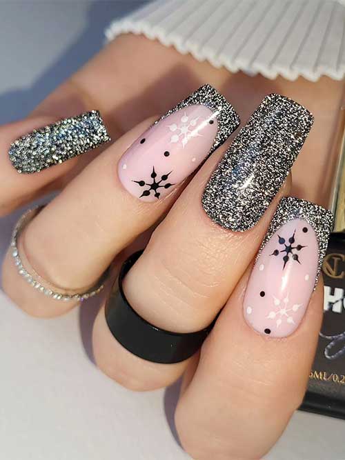 Uñas de invierno negras brillantes adornadas con purpurina dorada y dos uñas decorativas de punta francesa con copos de nieve blancos y negros.